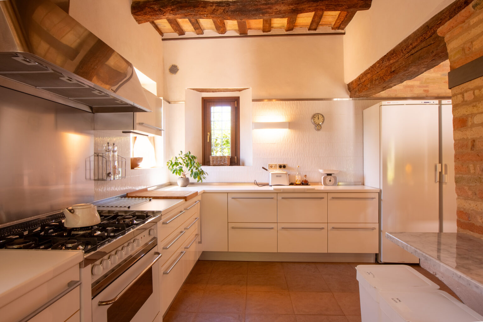 Modern kitchen with white cabinetry, stainless steel appliances, and wooden beams, featuring a bright window and a clean, minimalist design. | Only on SopranoVillas