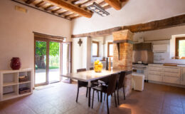 Bright and airy kitchen dining area featuring a wooden table surrounded by chairs, large windows with views of greenery, rustic wooden beams, and modern appliances. Ideal for family gatherings and meals.