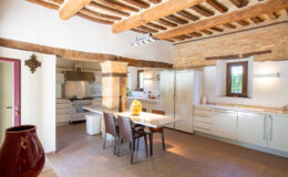 Spacious modern kitchen featuring rustic wooden beams, a marble dining table, and stainless steel appliances. The design combines contemporary elements with traditional accents, creating a warm and inviting atmosphere. Natural light streams through a window, illuminating the elegant decor and inviting dining space.