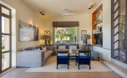 Spacious and modern living room featuring a comfortable gray sectional sofa, blue accent chairs, and a large window with a view of the outdoors. Decorated with artwork, a coffee table, and stylish lamps, the room exudes a relaxed ambiance perfect for entertaining or unwinding.