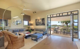 Spacious and bright living room featuring comfortable seating, a modern ceiling fan, and large windows that open to a scenic outdoor patio. The decor includes a stylish coffee table with a chess set and artwork on the walls, creating a welcoming atmosphere for relaxation and entertainment.