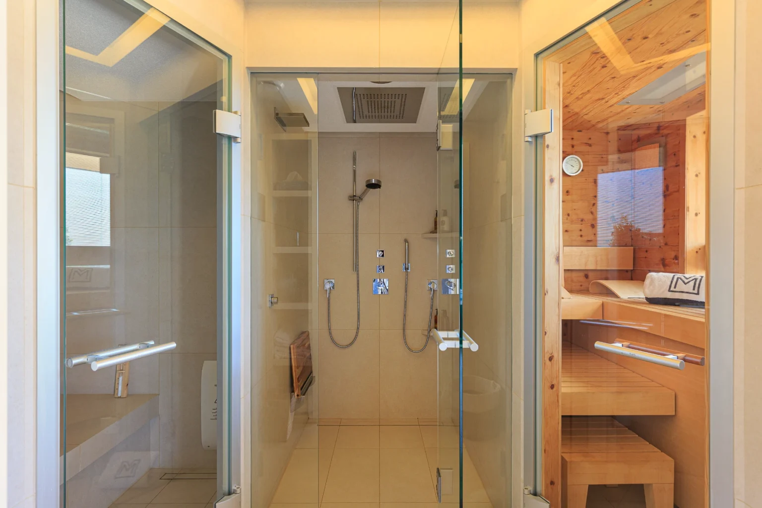 Modern bathroom featuring two glass-enclosed shower areas, one with a rainfall showerhead and the other with wooden accents, showcasing a sleek design and spacious layout. | Only on SopranoVillas