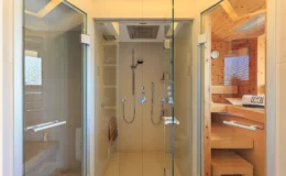Modern bathroom featuring two glass-enclosed shower areas, one with a rainfall showerhead and the other with wooden accents, showcasing a sleek design and spacious layout.