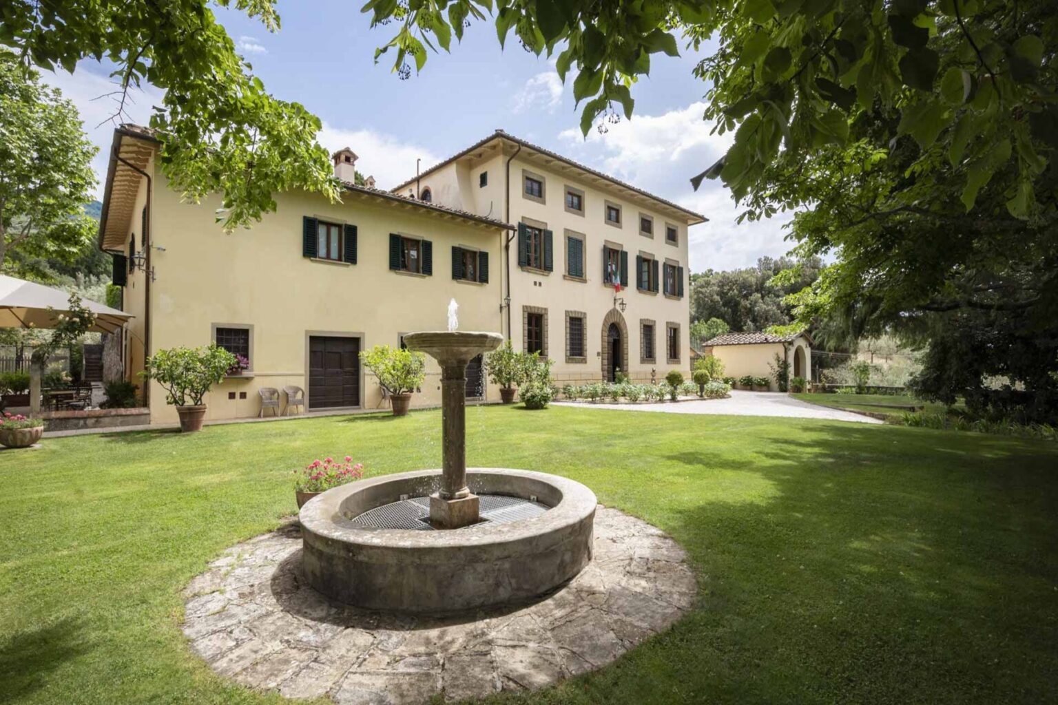 Elegant villa surrounded by lush greenery, featuring a central stone fountain and well-maintained gardens, ideal for outdoor gatherings and relaxation. | Only on SopranoVillas