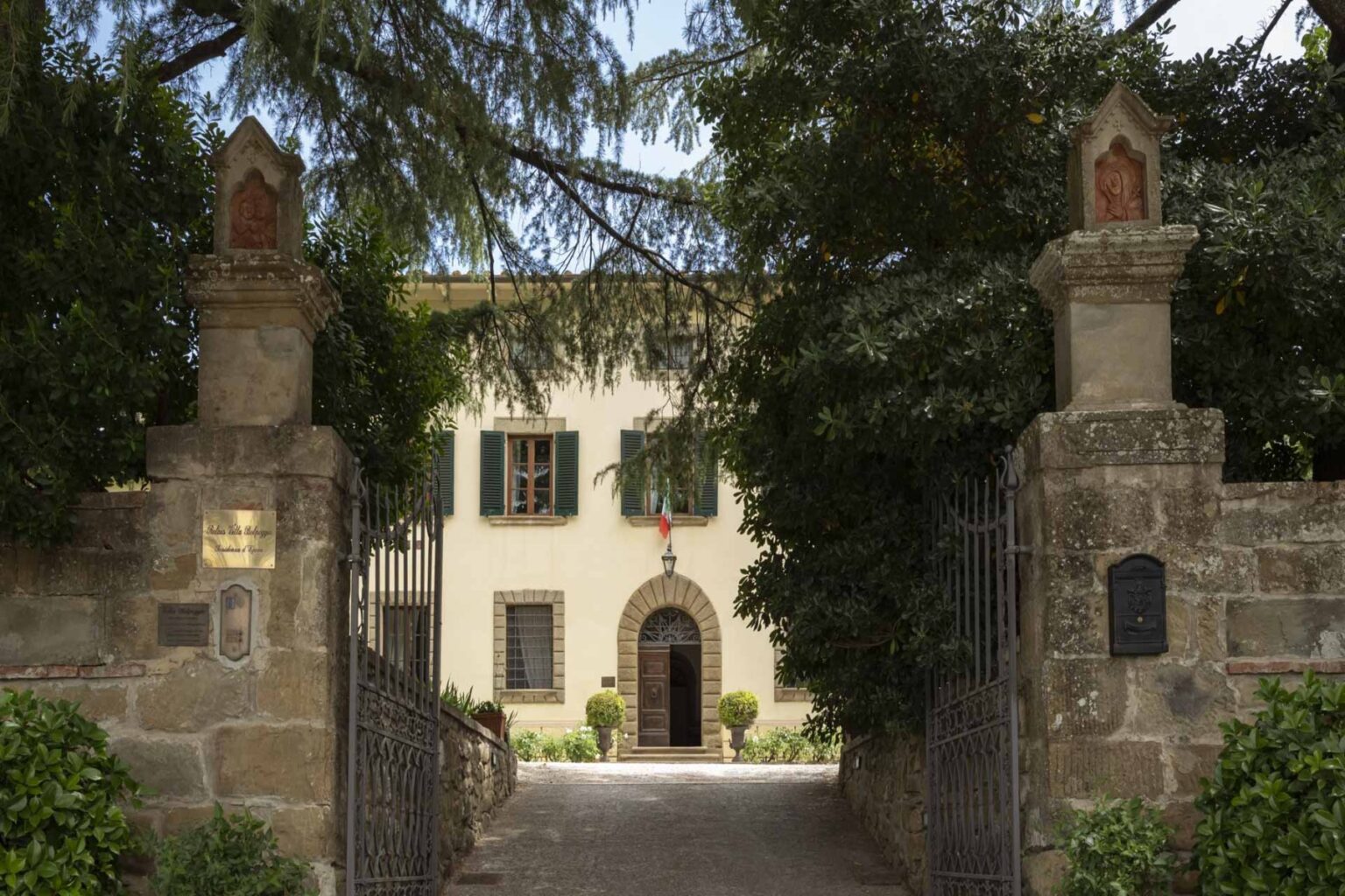 Historic villa entrance with stone gateposts and lush greenery, leading to a charming building featuring traditional architecture and decorative elements. Ideal for showcasing Italian heritage and architectural beauty. | Only on SopranoVillas
