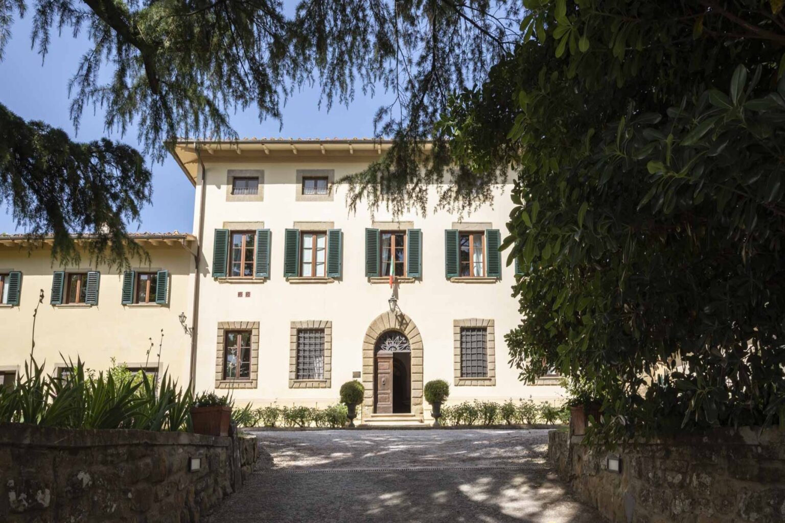 Historic villa with classic architecture, featuring a white facade, green shutters, and a landscaped entrance, surrounded by trees and gardens. Ideal for tourism and cultural heritage exploration. | Only on SopranoVillas