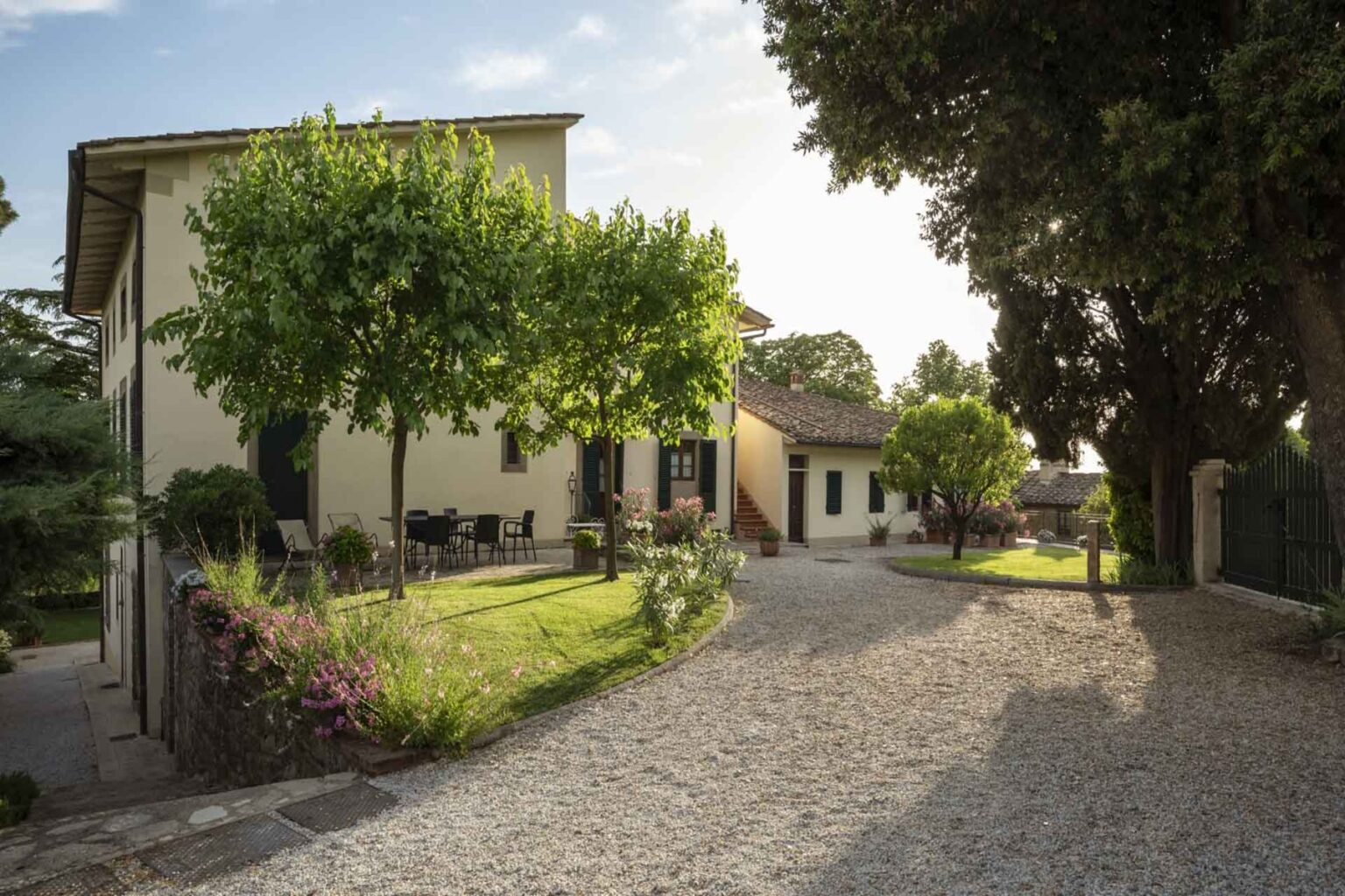 Charming countryside villa surrounded by lush greenery, featuring a gravel driveway and outdoor seating area, perfect for relaxation and enjoying nature. | Only on SopranoVillas