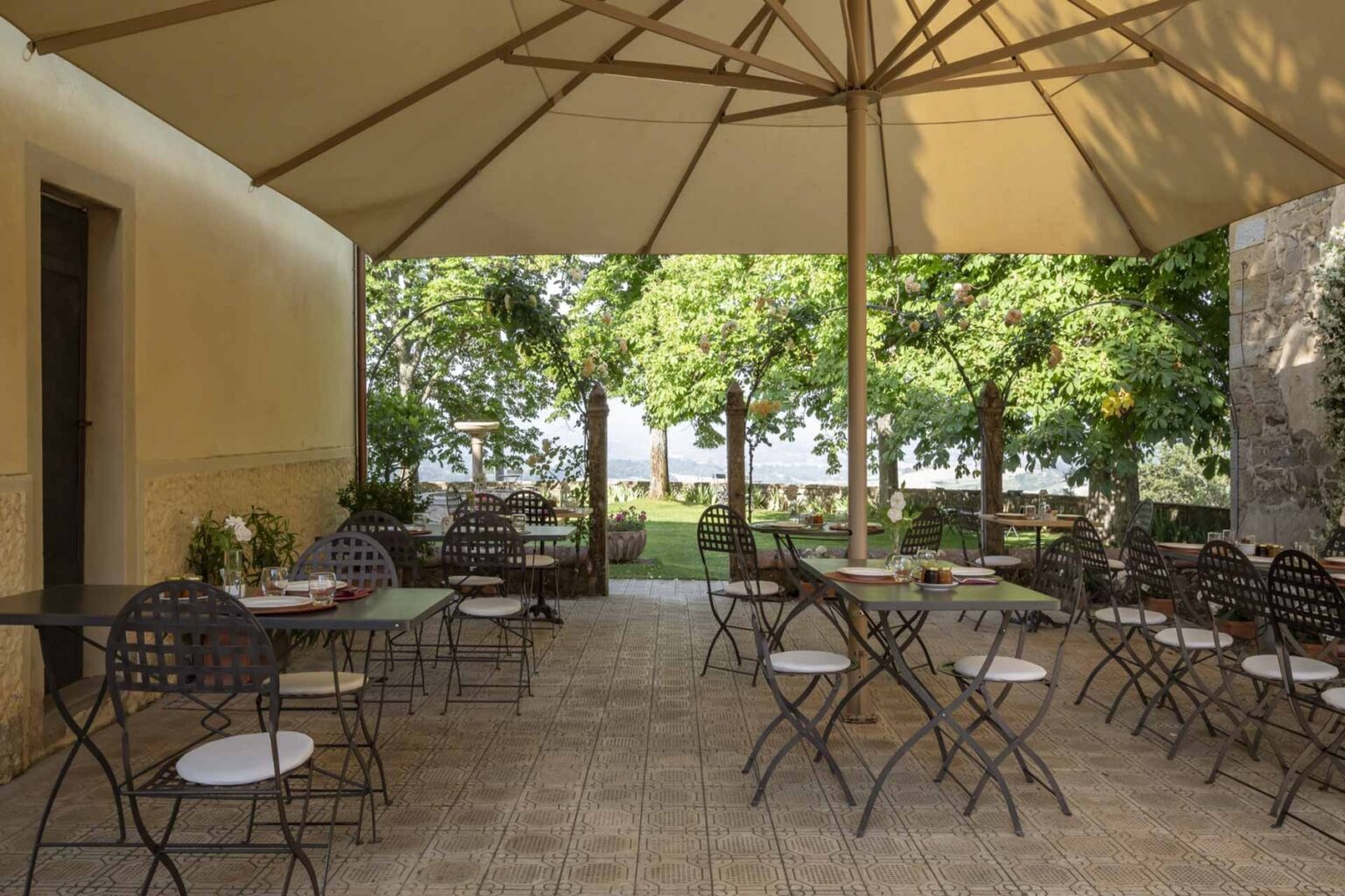 Outdoor dining area with metal tables and chairs under a large canopy, surrounded by greenery and a scenic view. Ideal for al fresco meals and gatherings. | Only on SopranoVillas