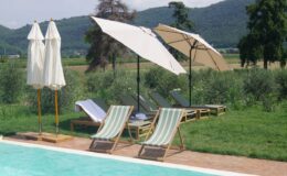 Relaxing outdoor pool area featuring comfortable lounge chairs and large umbrellas, surrounded by lush greenery and scenic hills, ideal for leisure and sunbathing.