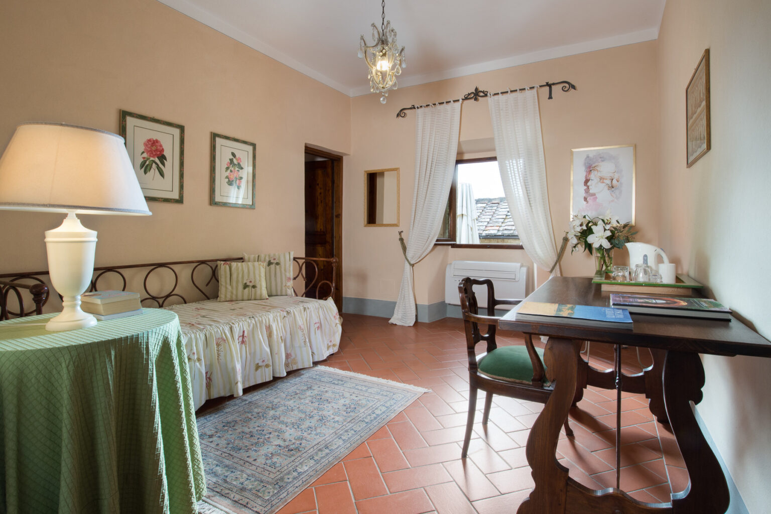 Cozy interior of a stylish living room featuring a sofa, a decorative lamp, a wooden table with stationery, and artwork on the walls, illuminated by natural light from a window. | Only on SopranoVillas