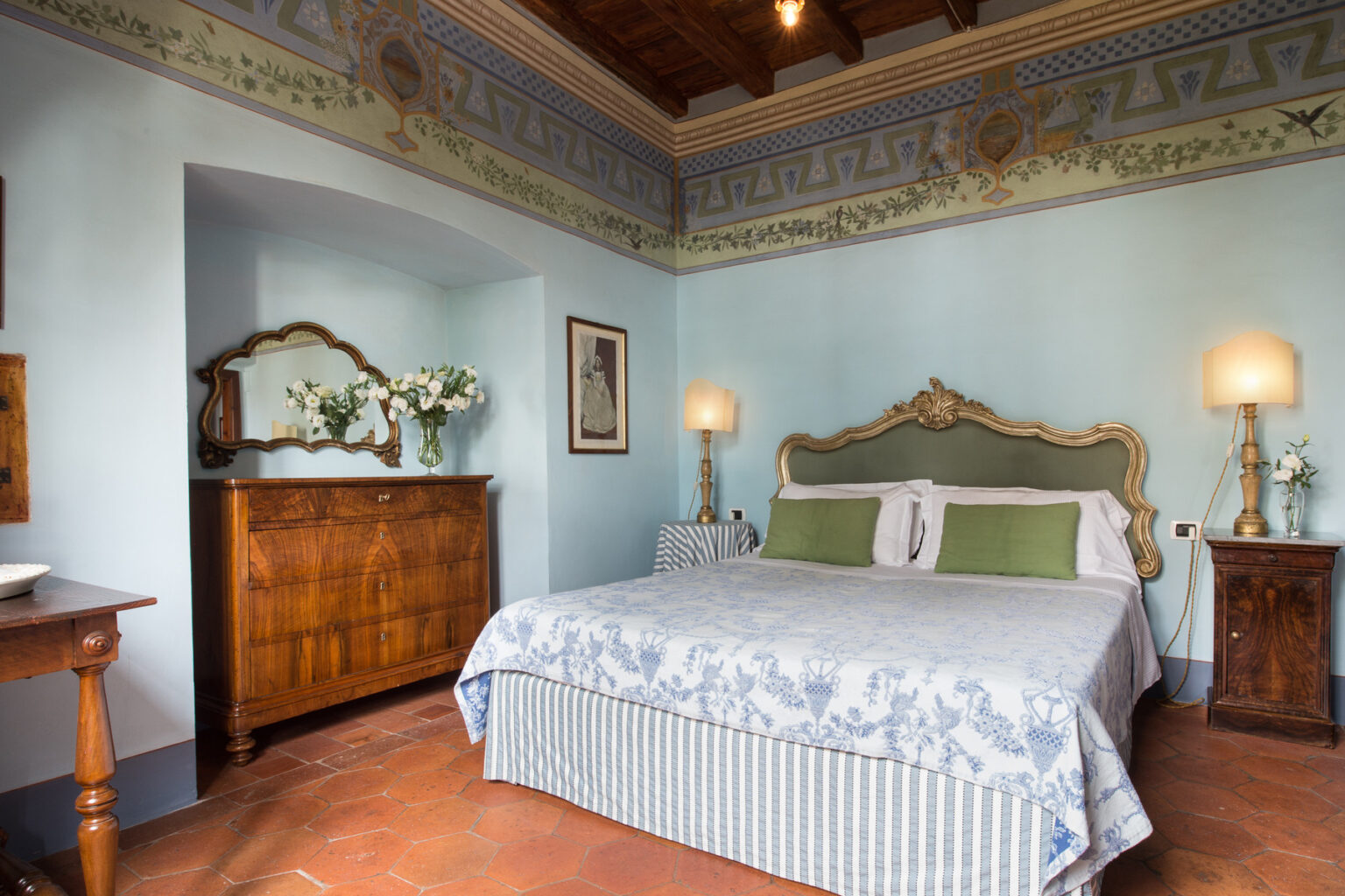 Elegant bedroom featuring a queen-sized bed with decorative pillows, vintage wooden furniture, and soft blue walls adorned with intricate ceiling designs. The room includes a stylish dresser and bedside lamps, creating a cozy and inviting atmosphere. Ideal for a relaxing getaway or home decor inspiration. | Only on SopranoVillas