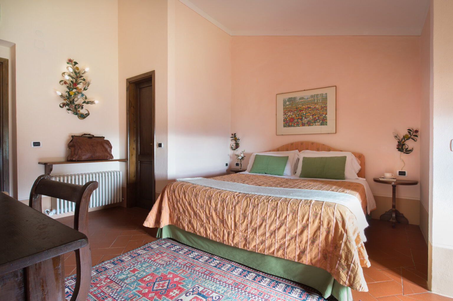 Cozy bedroom featuring a large bed with green and beige bedding, a wooden table, and decorative wall art. The room has peach-colored walls and warm lighting, creating a welcoming atmosphere. Ideal for relaxation and comfort. | Only on SopranoVillas