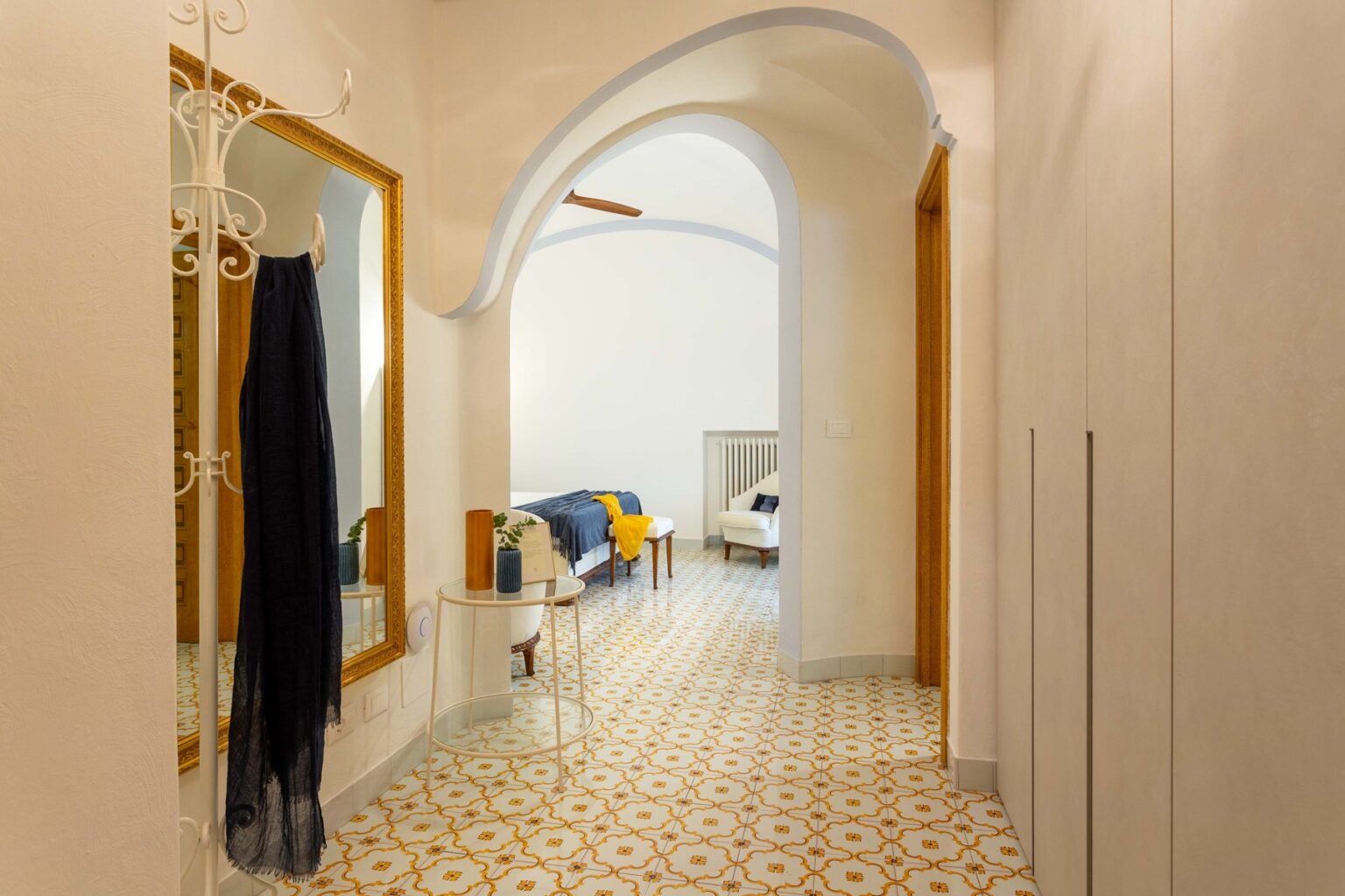 Bright and inviting hallway featuring an arched entrance, decorative mirror, stylish coat rack, and patterned tiled floor, leading to a cozy living area with colorful accents. | Only on SopranoVillas