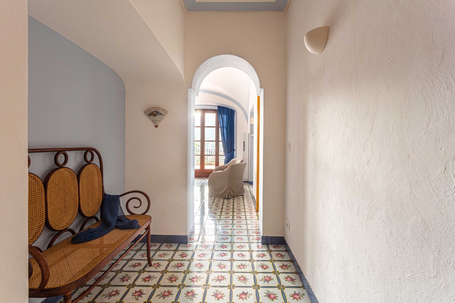 Interior hallway showcasing a traditional design with patterned tile flooring, a wooden bench, and a bright, inviting atmosphere leading to a cozy living area. | Only on SopranoVillas