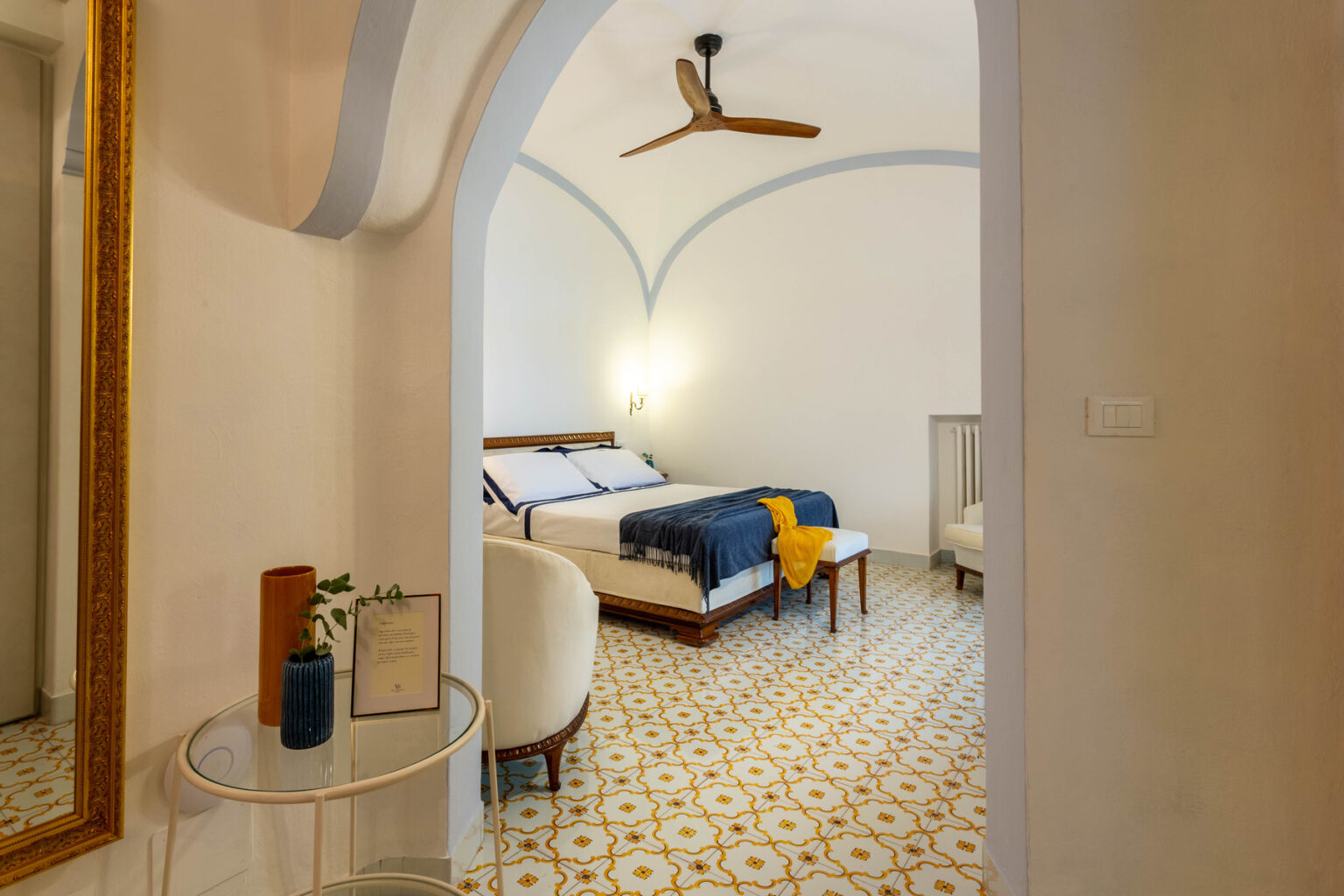 Spacious bedroom with a ceiling fan, featuring a comfortable bed, decorative throw, and stylish patterned floor tiles, viewed from an arched doorway. | Only on SopranoVillas
