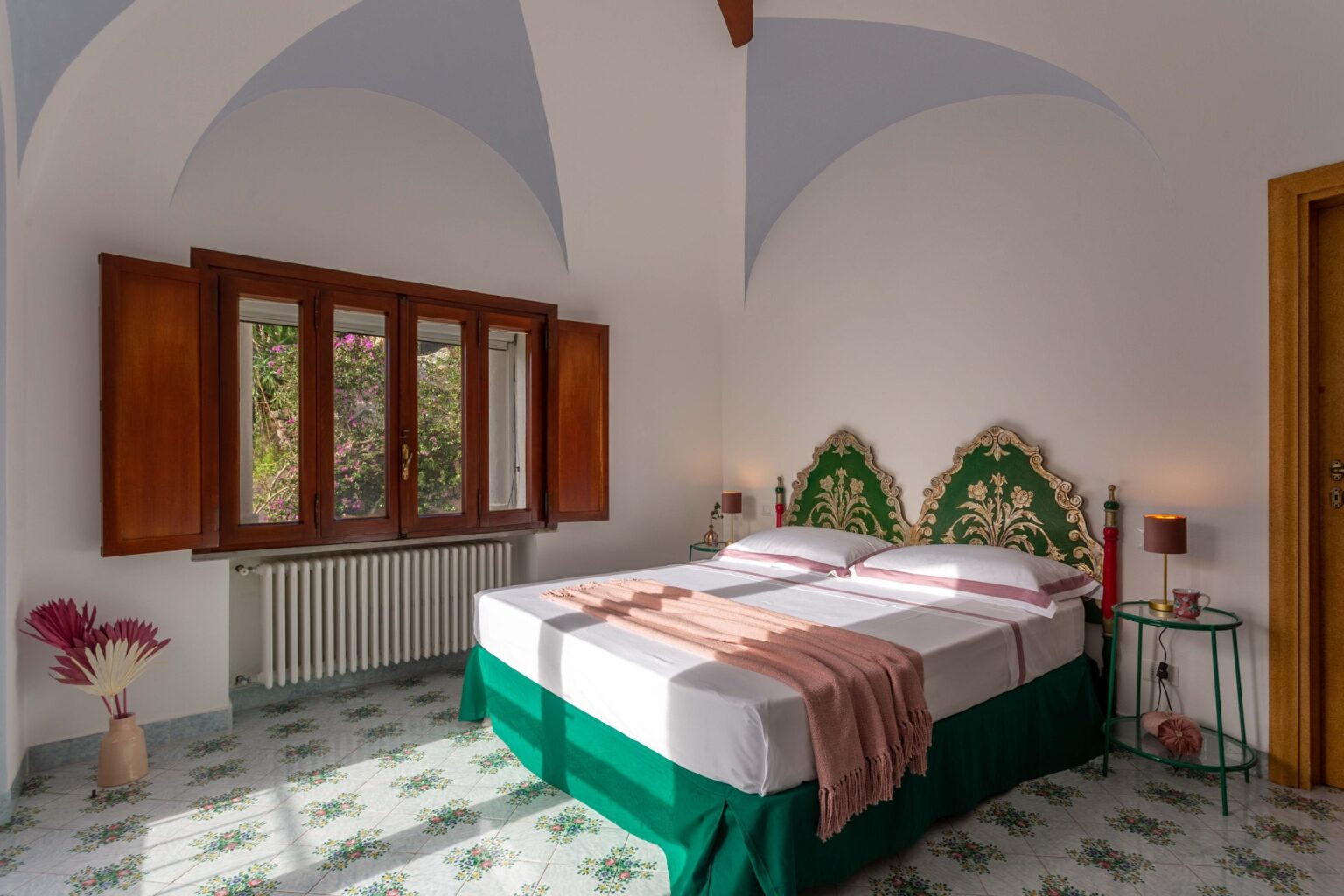Bright and airy bedroom featuring a green and white bed with decorative headboard, large windows with wooden shutters, and elegant decor, perfect for a relaxing getaway. | Only on SopranoVillas