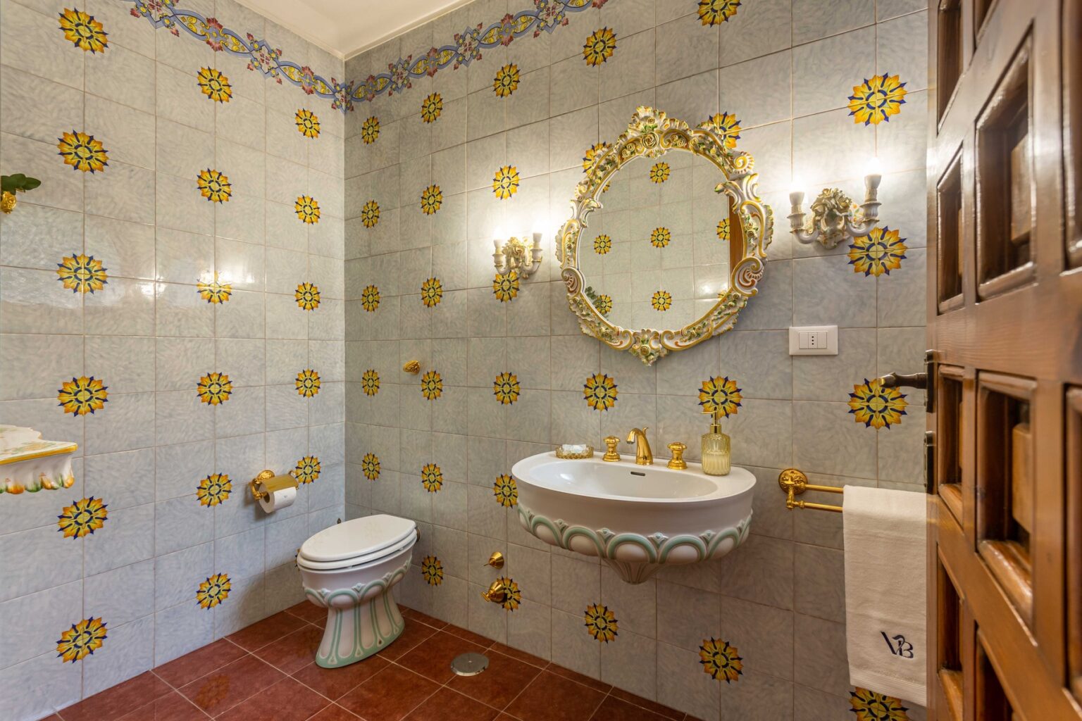 Elegant bathroom featuring decorative yellow floral tiles, a vintage-style mirror, and gold fixtures, showcasing a blend of classic and modern design elements. | Only on SopranoVillas