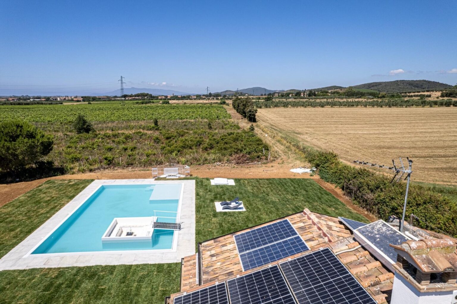 Aerial view of a modern villa featuring a swimming pool and solar panels, surrounded by lush vineyards and golden fields under a clear blue sky. | Only on SopranoVillas