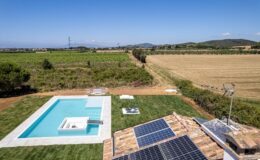 Aerial view of a modern villa featuring a swimming pool and solar panels, surrounded by lush vineyards and golden fields under a clear blue sky.