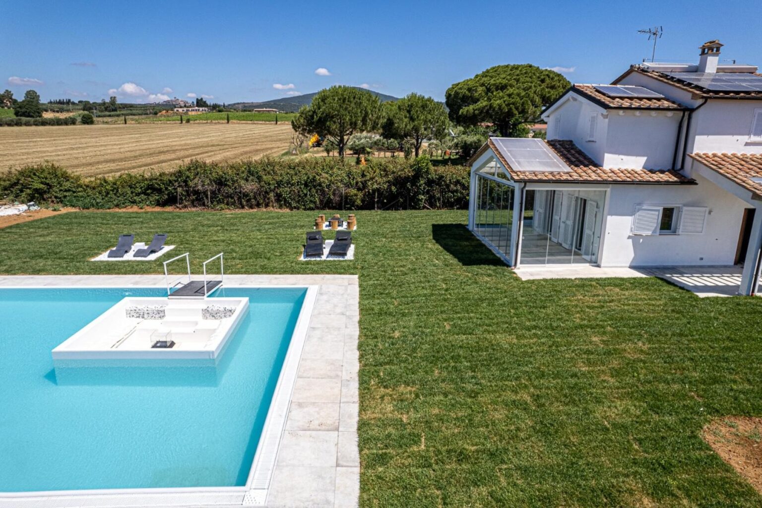 Modern villa with a swimming pool and sun loungers in a lush green garden, surrounded by scenic countryside and clear blue skies. Ideal for relaxation and outdoor living. | Only on SopranoVillas