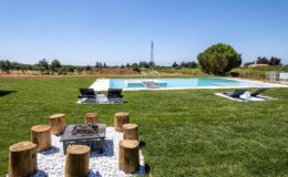 Outdoor pool area featuring a well-maintained lawn, lounge chairs, and a cozy fire pit surrounded by wooden stools, ideal for relaxation and gatherings.