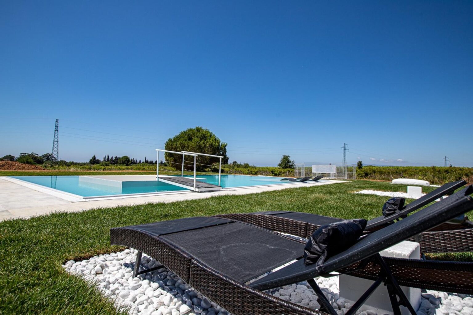 Luxury outdoor pool area with modern lounge chairs, surrounded by lush greenery and clear blue sky, perfect for relaxation and leisure. | Only on SopranoVillas