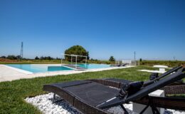 Luxury outdoor pool area with modern lounge chairs, surrounded by lush greenery and clear blue sky, perfect for relaxation and leisure.