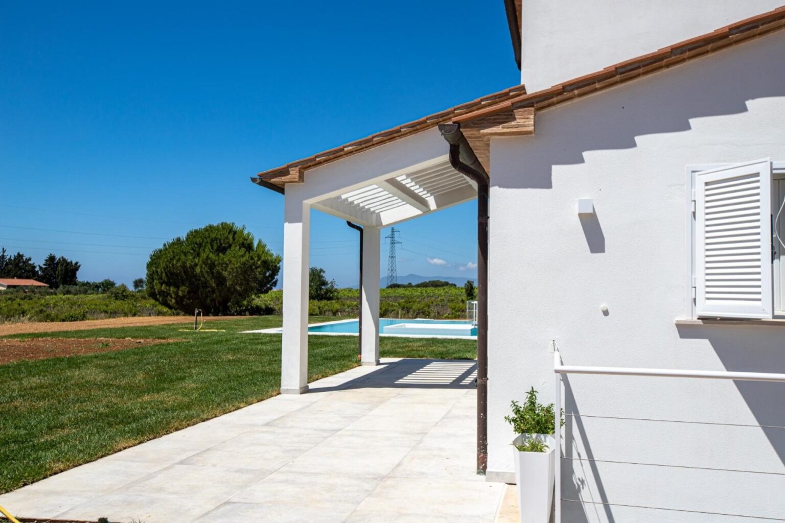 Modern white house exterior with an open porch, overlooking a green lawn and swimming pool under a clear blue sky. | Only on SopranoVillas