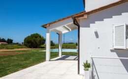 Modern white house exterior with an open porch, overlooking a green lawn and swimming pool under a clear blue sky.