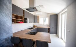 Modern kitchen featuring sleek gray cabinets, a wooden island with a built-in cooktop, and large windows for natural light.