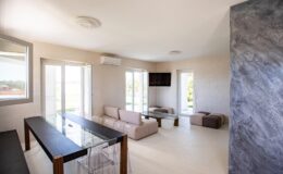 Modern living room with large windows, neutral-colored walls, a comfortable sofa, and a sleek glass table, creating a bright and airy atmosphere.