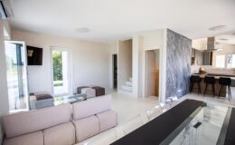 Modern open-concept living room and dining area with stylish furniture, large windows, and a contemporary kitchen in a bright, airy home.