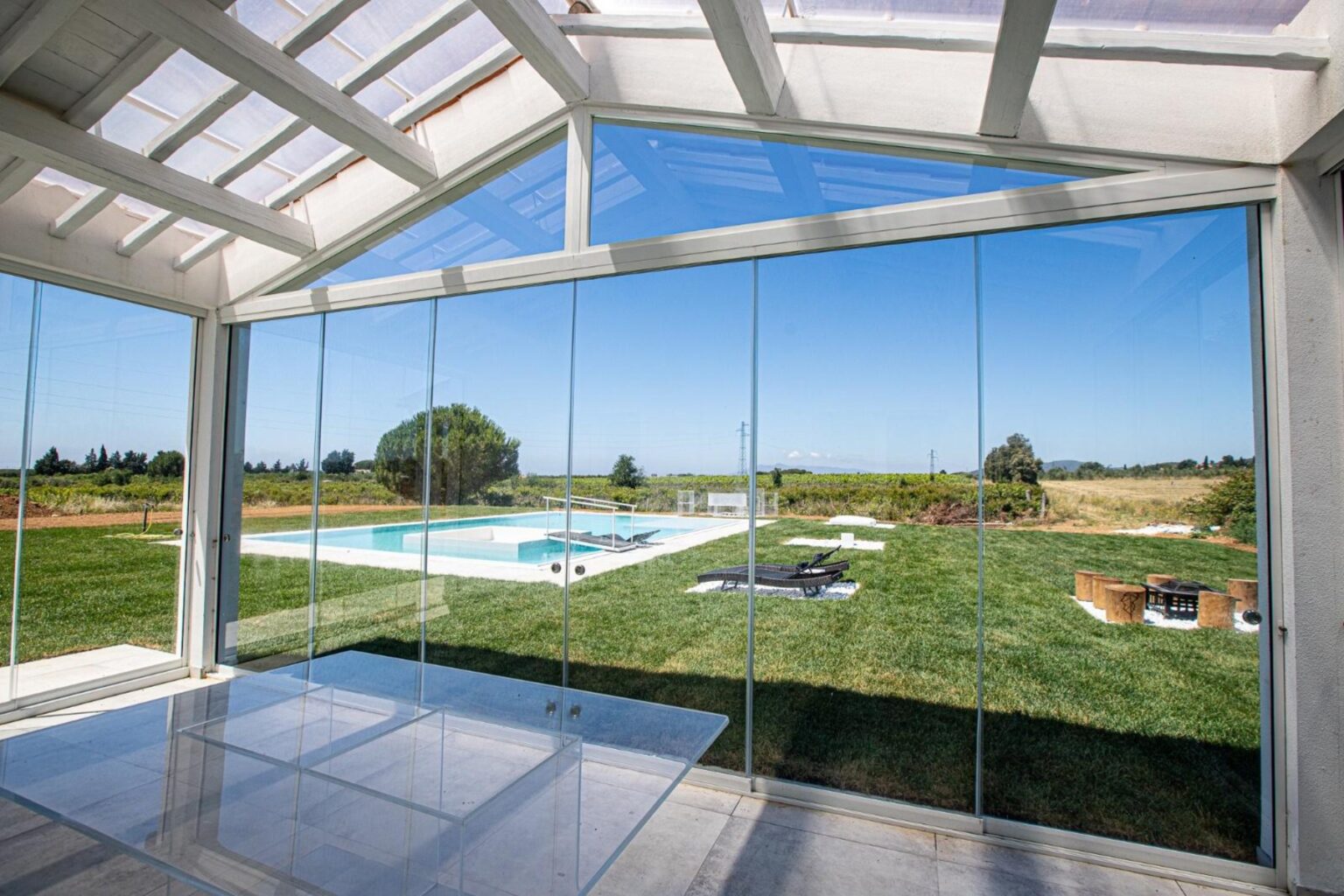 Modern glass wall overlooking a serene outdoor pool and lush green landscape, showcasing a bright and airy interior space with natural light. | Only on SopranoVillas