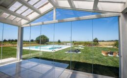 Modern glass wall overlooking a serene outdoor pool and lush green landscape, showcasing a bright and airy interior space with natural light.