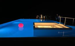 Modern swimming pool at night with illuminated blue water, featuring a bright red floating ball and a spa area.