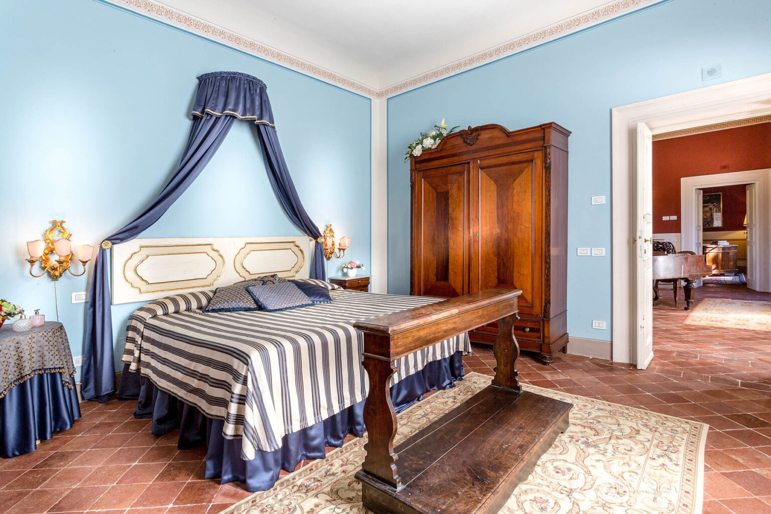 Elegant bedroom featuring a striped bedspread, blue walls, and classic wooden furniture. The room includes a stylish wooden wardrobe and decorative accents, creating a cozy and inviting atmosphere. | Only on SopranoVillas