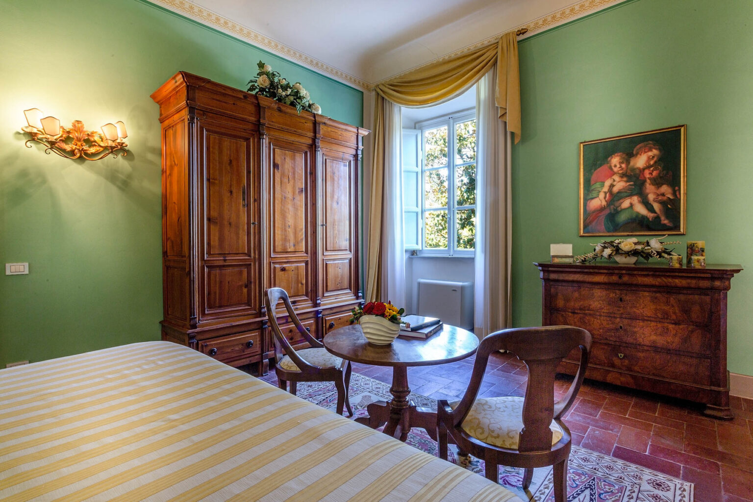 Cozy bedroom with green walls, antique wooden furniture, a small dining table, and a window letting in natural light, featuring a classic painting on the wall. | Only on SopranoVillas