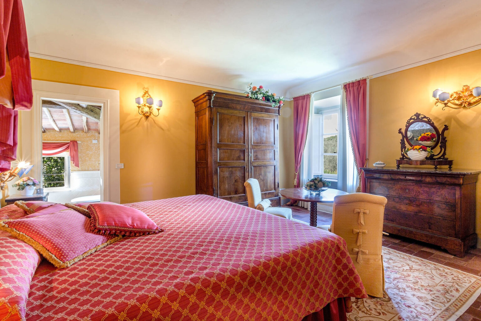 Cozy and elegantly decorated bedroom featuring a large red quilted bedspread, warm yellow walls, antique wooden furniture, and natural light streaming through the windows, creating a welcoming atmosphere for guests. | Only on SopranoVillas