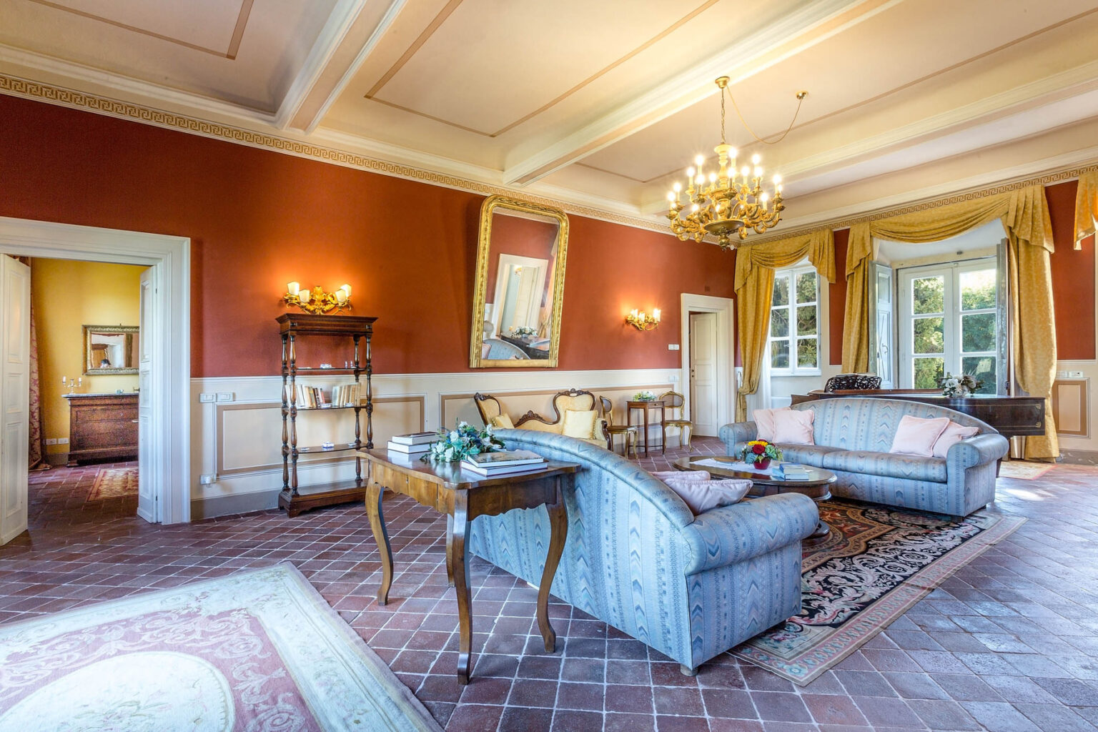 Elegant living room interior featuring plush sofas, a chandelier, and rich red walls, complemented by warm lighting and decorative accents. | Only on SopranoVillas