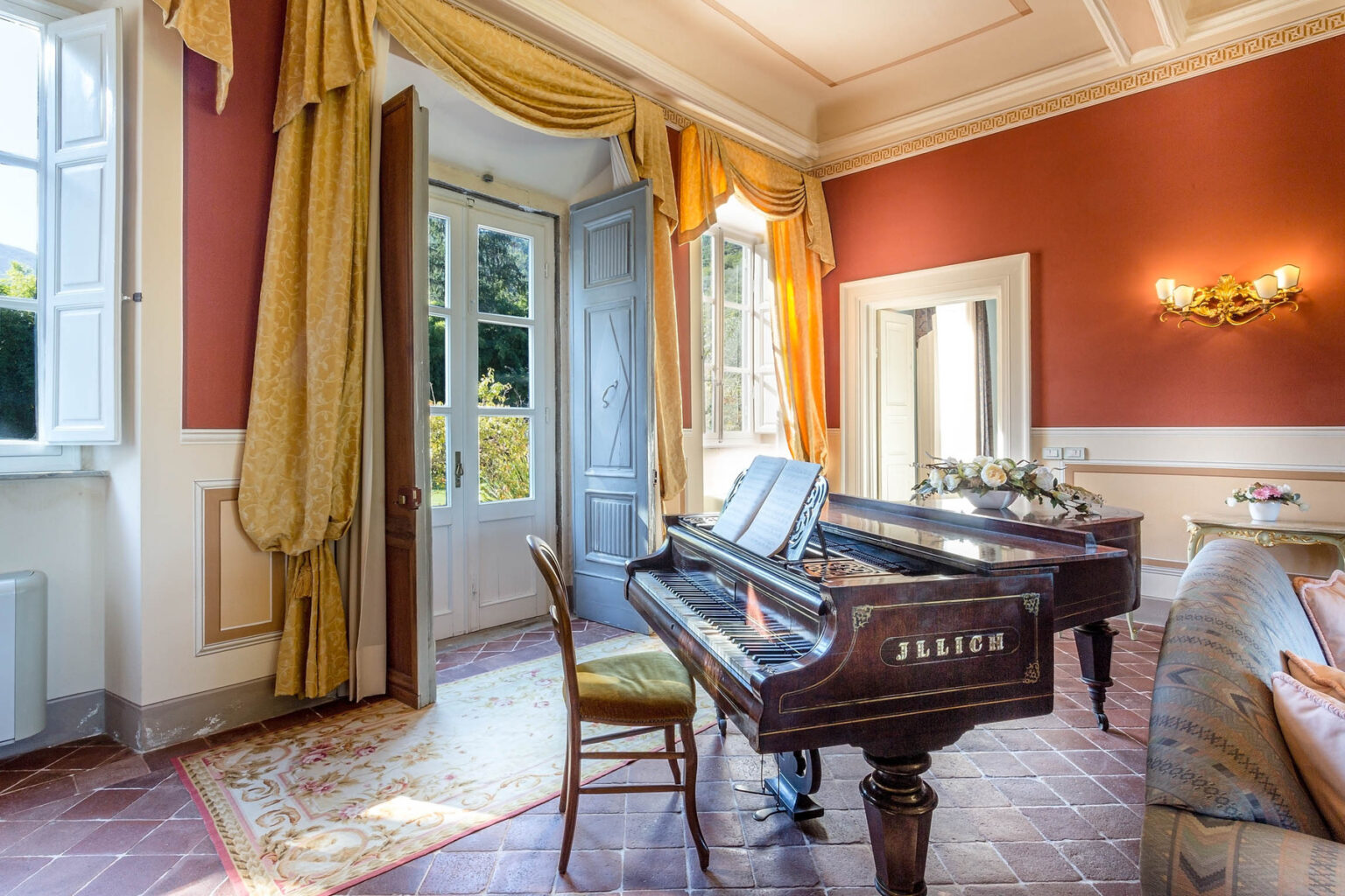 Elegant interior of a room featuring a grand piano, vintage chair, and large windows with golden drapes, creating a warm and inviting atmosphere. | Only on SopranoVillas
