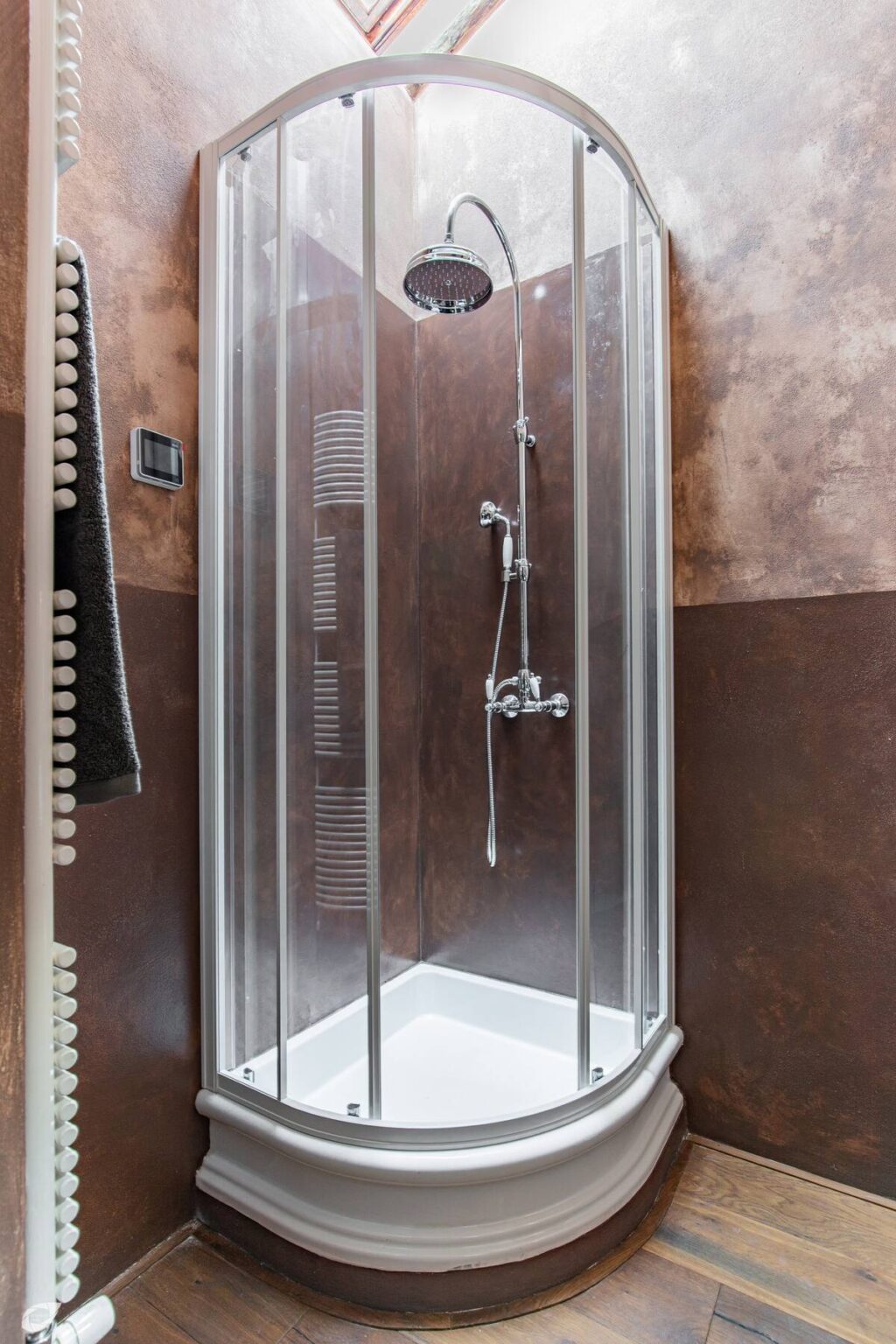 Modern shower enclosure with sleek glass doors and chrome fixtures, set against a stylish brown textured wall. Designed for contemporary bathrooms, featuring a rainfall showerhead and a minimalist aesthetic. | Only on SopranoVillas