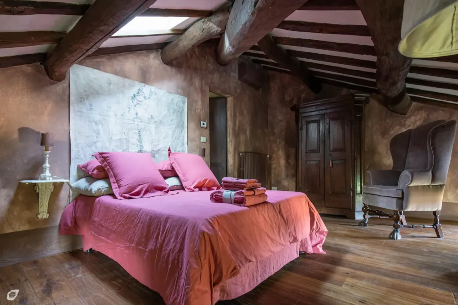 Cozy bedroom with a rustic design featuring a pink bedspread, plush pillows, wooden beams, and a vintage wardrobe, illuminated by natural light. Perfect for a relaxing getaway. | Only on SopranoVillas