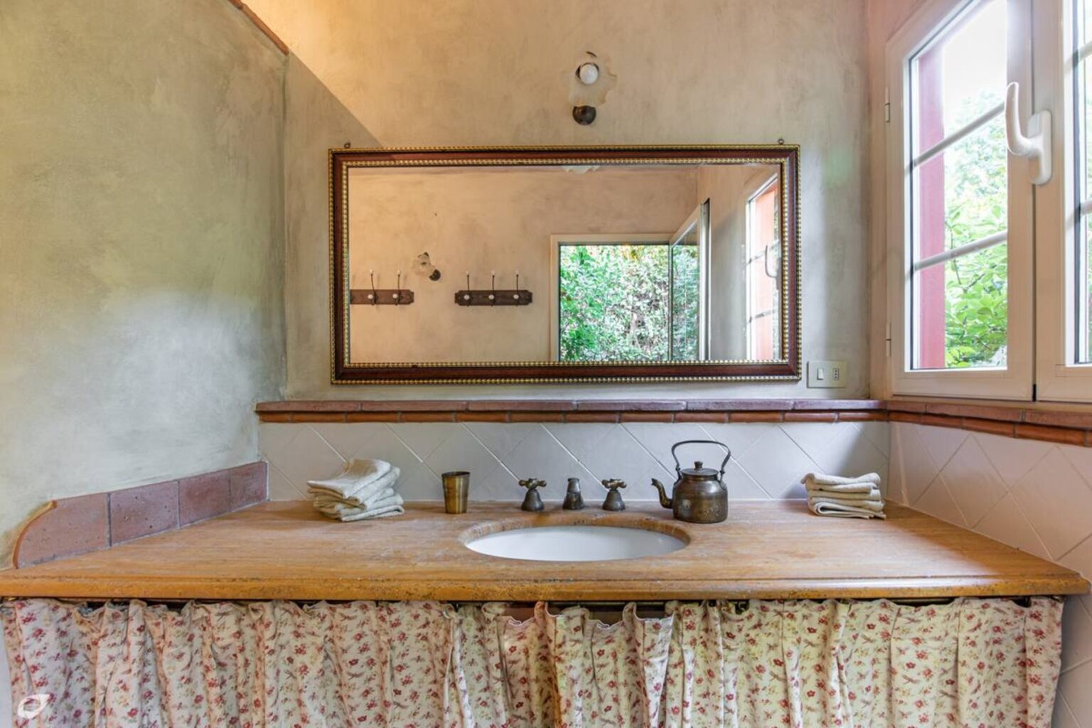 Modern bathroom interior featuring a wooden vanity with a sink, decorative curtain, and a large mirror reflecting natural light from a nearby window. | Only on SopranoVillas