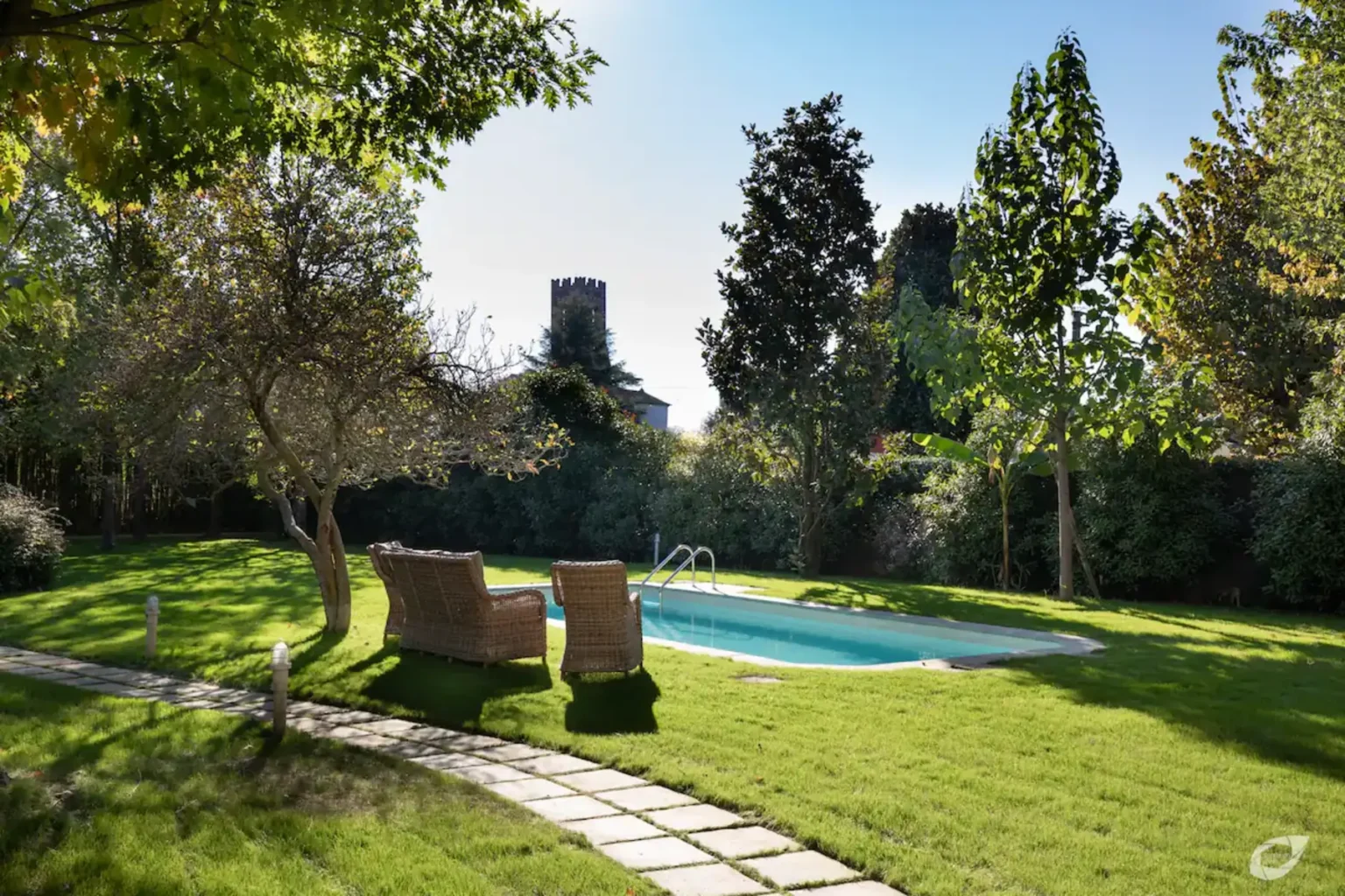 Serene backyard with a swimming pool, surrounded by lush greenery and tall trees, featuring two comfortable lounge chairs on a well-manicured lawn. | Only on SopranoVillas