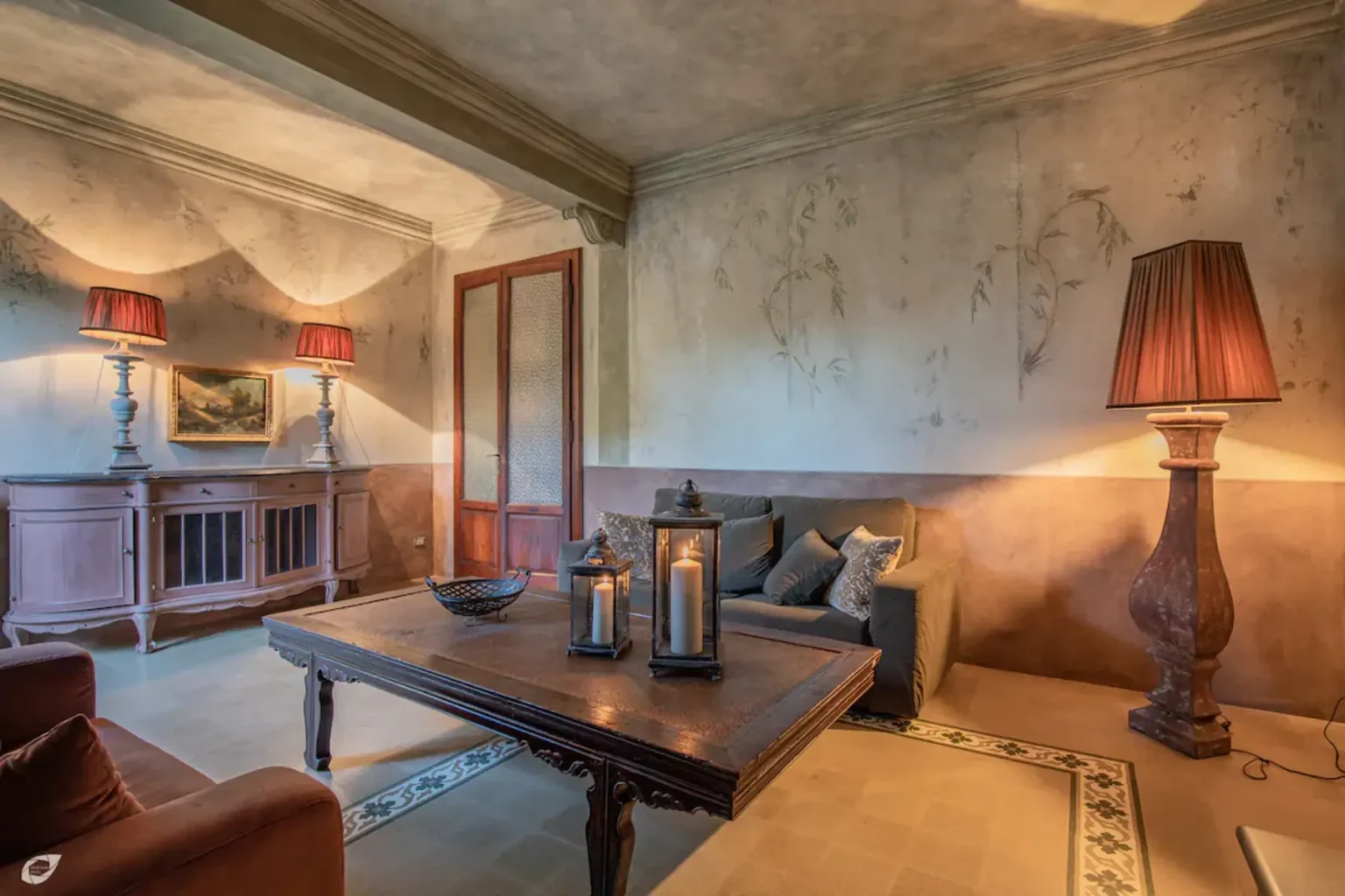 Cozy living room interior featuring a wooden table, decorative lanterns, stylish lamps, and vintage decor against a textured wall. | Only on SopranoVillas