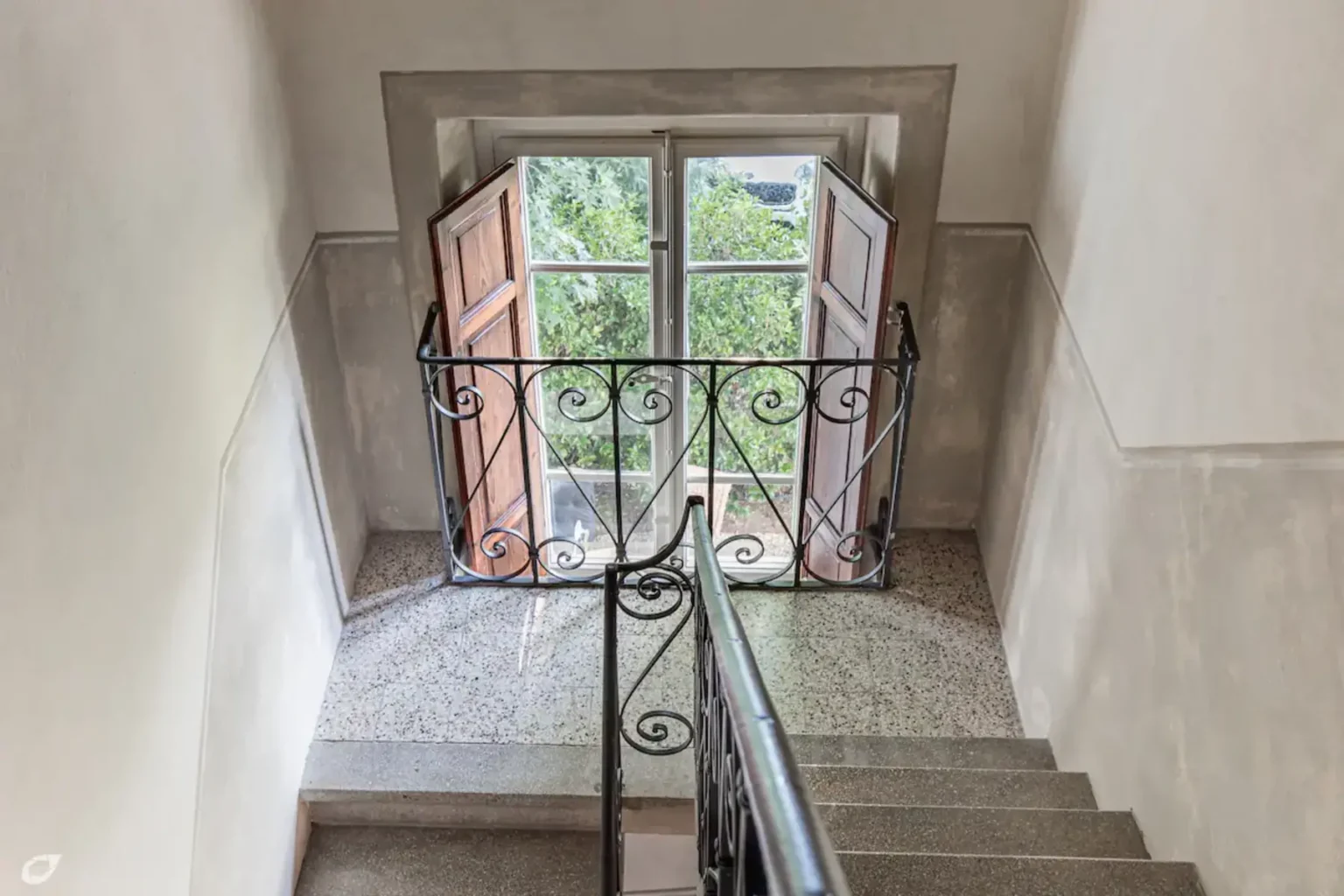 Staircase leading to an open window with wooden shutters, featuring a decorative metal railing and a view of greenery outside. | Only on SopranoVillas