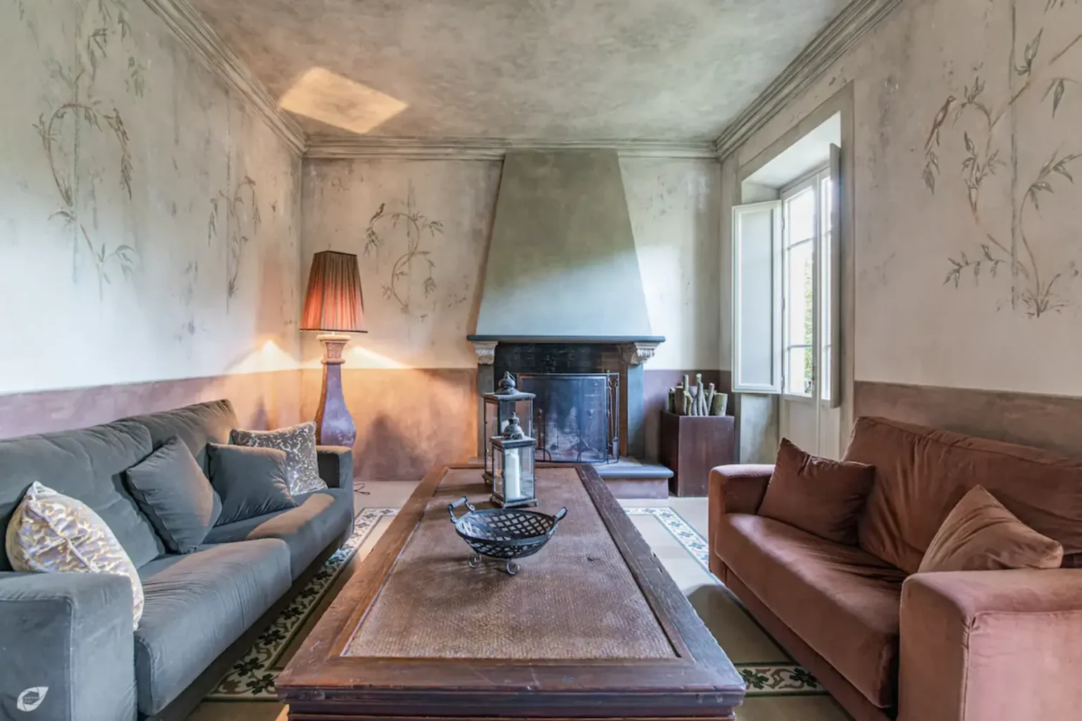 Cozy living room featuring a fireplace, comfortable sofas in muted tones, a stylish table with decorative items, and large windows allowing natural light to brighten the space. | Only on SopranoVillas