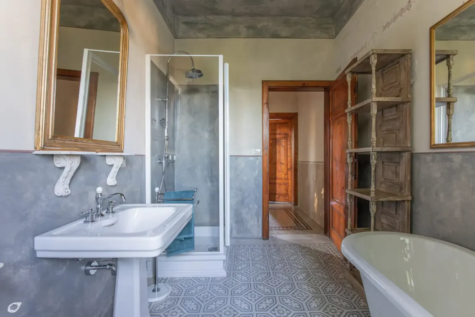 Modern bathroom featuring a glass shower, white sink, and freestanding bathtub, with stylish mirrors and wooden shelving, showcasing a blend of contemporary and rustic design elements. | Only on SopranoVillas