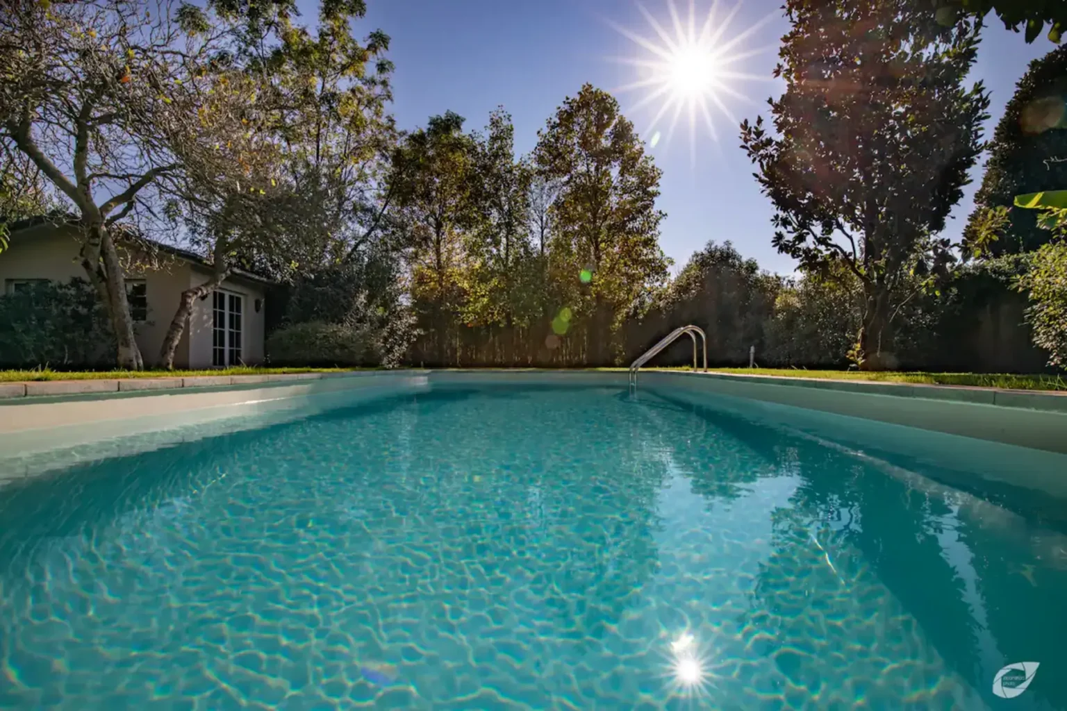 A sparkling blue swimming pool surrounded by lush greenery and trees, with bright sunlight shining overhead. | Only on SopranoVillas