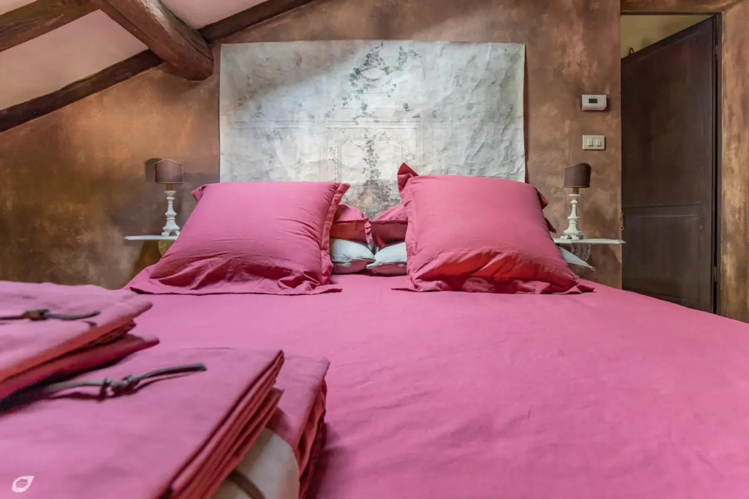 Cozy bedroom featuring a pink bedspread and matching pillows, complemented by rustic wooden beams and a decorative wall hanging. The scene exudes warmth and comfort, ideal for a relaxing retreat. | Only on SopranoVillas